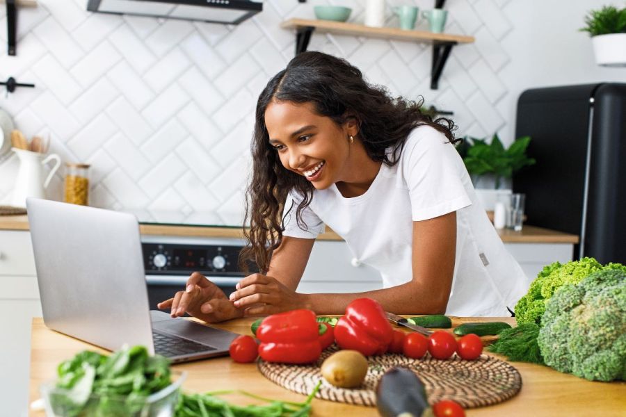 woman looking on laptop preparing healthy vegetables meal