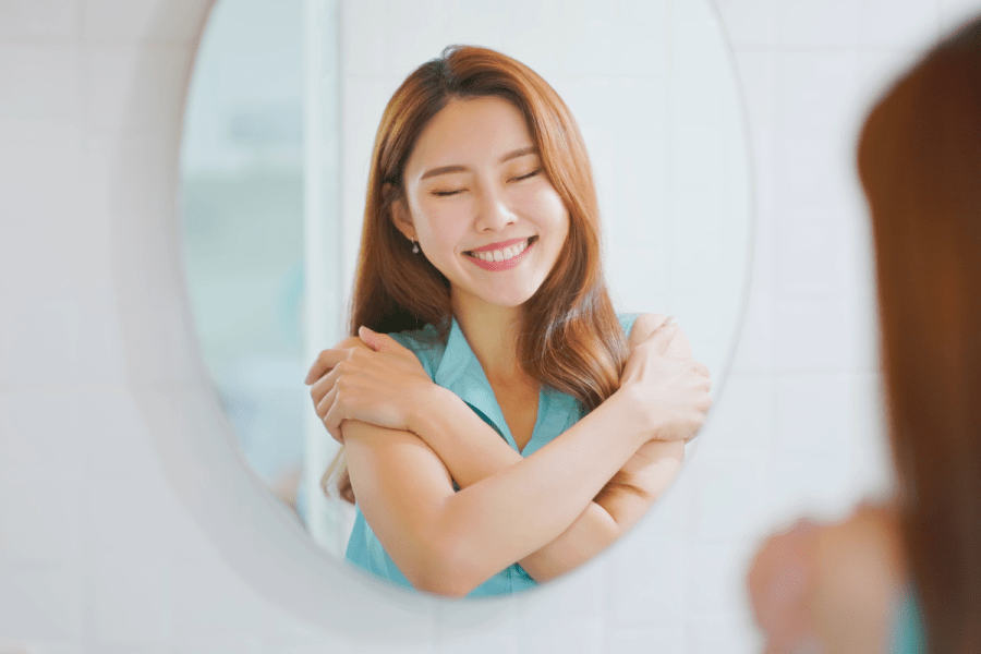 a woman smiling at herself in the mirror while practicing self-compassion