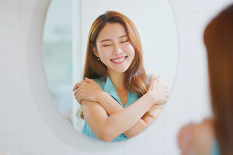 a woman smiling at herself in the mirror while practicing self-compassion