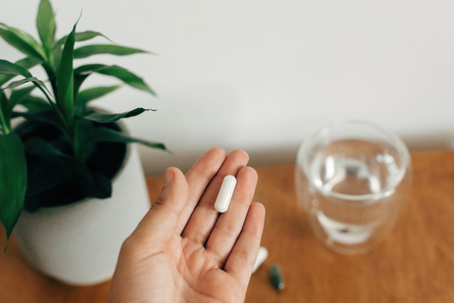 A photograph of a hand holding a magnesium pill, with a glass of water in the background