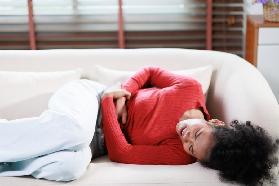 woman laying down on her sofa, clutching her stomach in pain