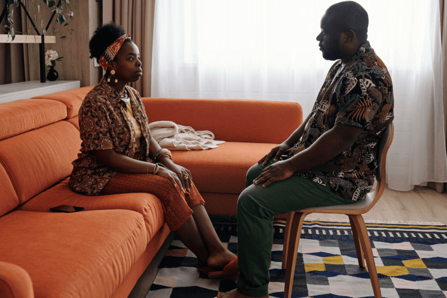 a couple sitting to have a discussion. They are facing each other, a woman on a couch and a man on a chair.