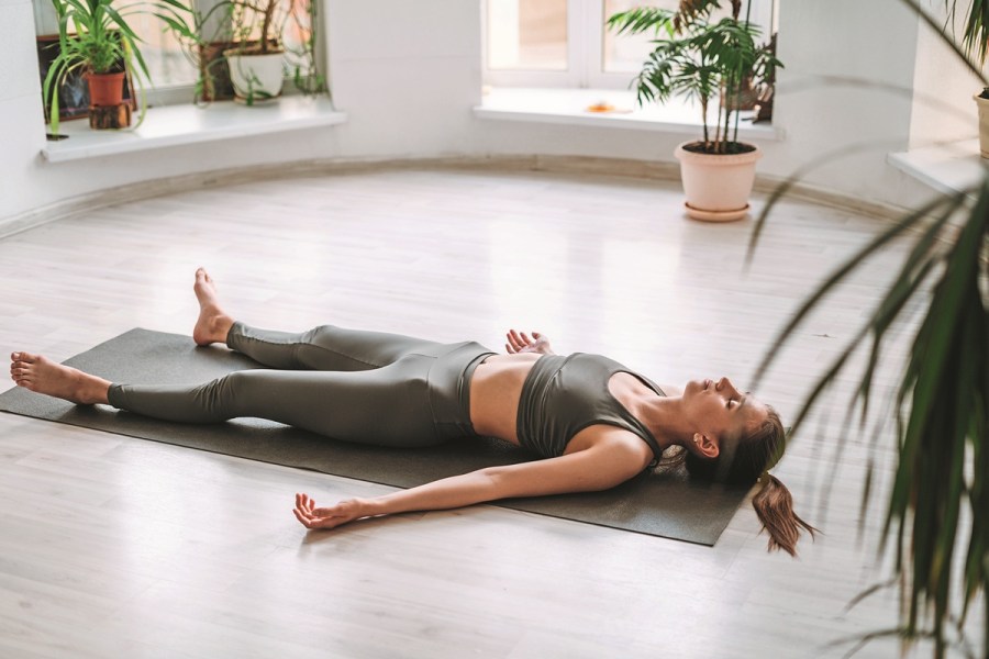Young fit woman practice yoga doing savasana in light yoga studio with green house plant