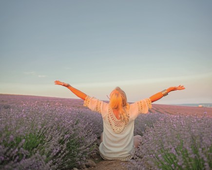 Back view of Middle-aged woman dressed boho style clothes, older female breath the healthy air in the field of lavender against the sun