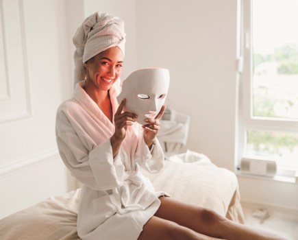 Beautiful young woman getting a led light therapy mask treatment for her face at the beauty salon.