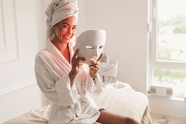 Beautiful young woman getting a led light therapy mask treatment for her face at the beauty salon.