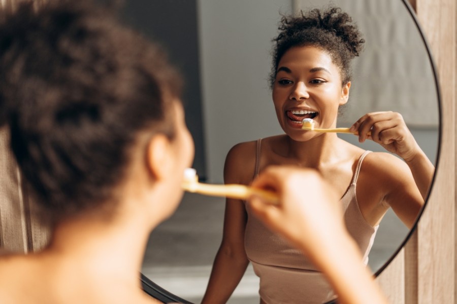 Happy,Young,Woman,Brushing,Her,Teeth,Looking,At,Her,Reflection