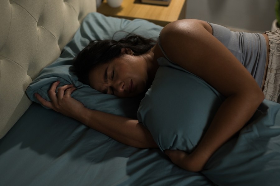 Distressed,Hispanic,Woman,Is,Lying,In,Bed,And,Hugging,Pillow,